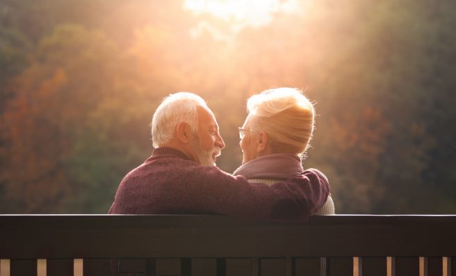 Senior couple sitting on bench in autumn park and looking sunset