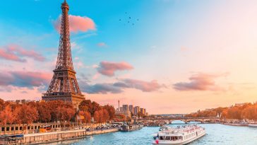 The main attraction of Paris and all of Europe is the Eiffel tower in the rays of the setting sun on the bank of Seine river with cruise tourist ships