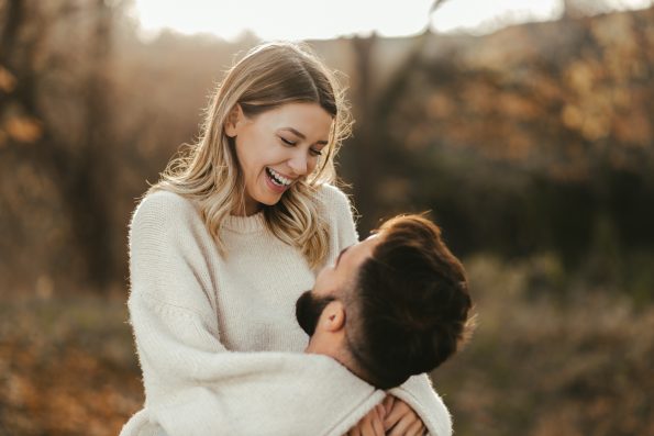 Young cheerful couple having fun  in nature during autumn. Woman being carried by her boyfriend