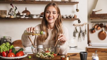 Image of joyful nice woman wearing casual clothes laughing while cooking dinner in cozy kitchen