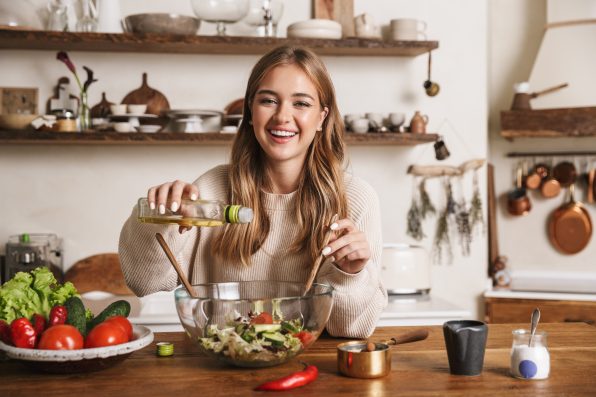 Image of joyful nice woman wearing casual clothes laughing while cooking dinner in cozy kitchen