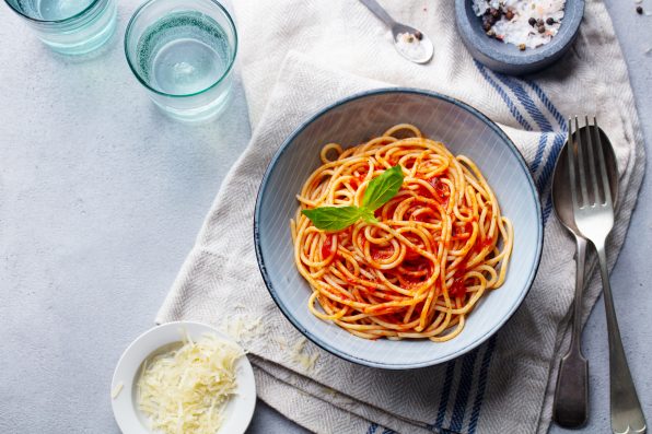 Pasta, spaghetti with tomato sauce and fresh basil in a bowl. Grey background. Top view. Copy space.