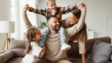 happy family mother father and kids play and laugh at home on   couch