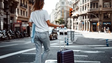 Young traveling woman with luggage on a sunny city street. Traveler on vacation. Waiting for taxi