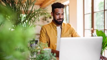 A young man with laptop and coffee working indoors, home office concept.