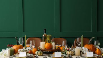 Autumn table setting with fresh pumpkins and flowers near green wall