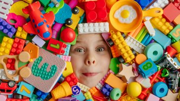 Little girl lying in the mess of toys. Top view, flat lay.