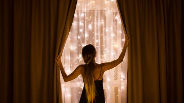 The girl opening the curtains behind which the window with Christmas illumination. Christmas holidays.