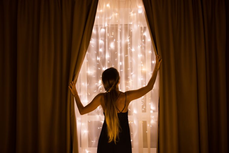 The girl opening the curtains behind which the window with Christmas illumination. Christmas holidays.