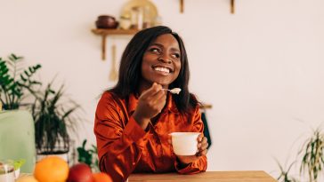 Beautiful young woman eating yogurt in the kitchen in the morning. Healthy food. Close up. Portrait shot