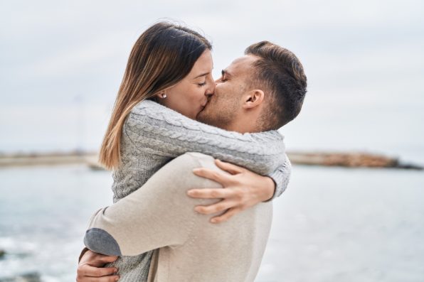 Man and woman couple hugging each other kissing at seaside