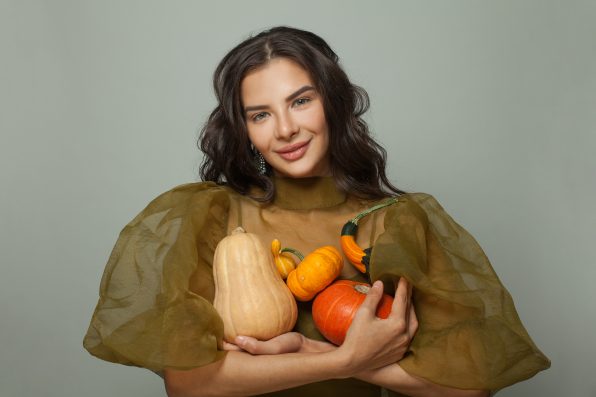 Cheerful young woman holding different orange pumpkins on white background. Thanksgiving or halloween portrait.