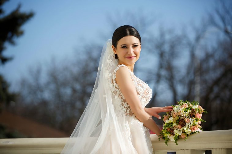 Happy beautiful young bride on the walk. Girl in a white dress with a veil. In the background are white pillars.