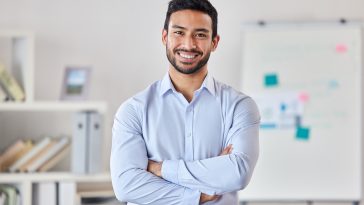 Smile, education and portrait of man teacher in a classroom or school and happy to study in a college or university. Academy, educator and young person or worker arms crossed and confident in class.