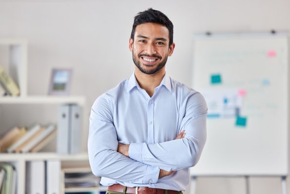 Smile, education and portrait of man teacher in a classroom or school and happy to study in a college or university. Academy, educator and young person or worker arms crossed and confident in class.