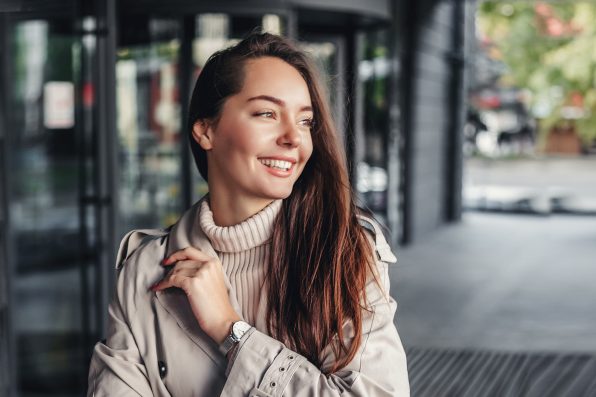 Portrait of a happy young woman against the background of an office building wearing a trench coat. copy space