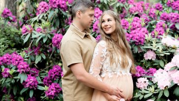 Hapy pregnant couple hugging in blossom garden. Future parents in blooming rhododendron park.