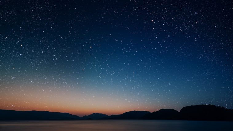 movement of stars in the night sky with the view of mountains.