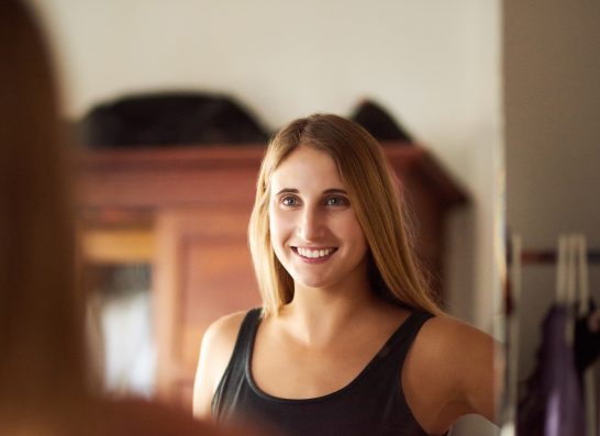 Woman, mirror and reflection in home for dressing, alone and ready in portrait with smile. Female person, glass window or happiness in house with change of clothes, casual or cool in New York City.