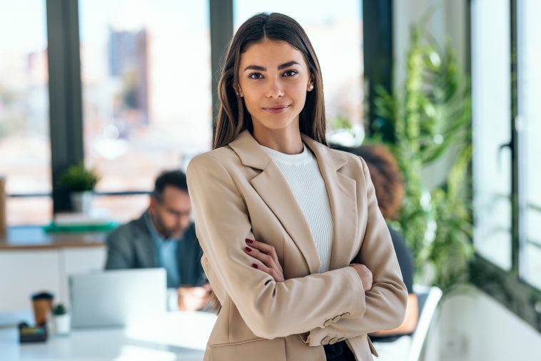 Portrait of beautiful young business woman standing while smiling looking at camera in the office