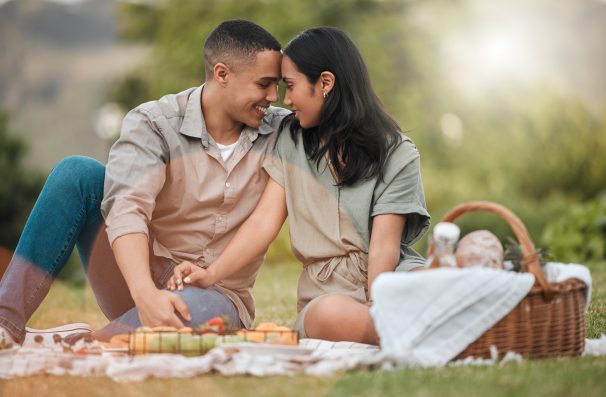 Connection, nature and couple on picnic for date with romance on vacation, getaway or weekend trip. Happy, basket and young man and woman with love, bonding and marriage activity in outdoor park