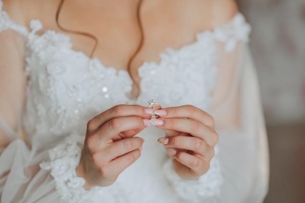 A woman is holding a ring in her hand. The ring is silver and has a diamond on it. The woman is wearing a white dress, and the dress is long and flowing. Concept of elegance and sophistication