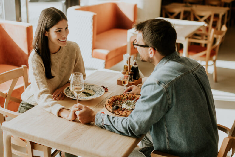 A couple enjoys a delightful evening, sharing dishes of flavorful cuisine and laughter while seated at a wooden table in a relaxed restaurant atmosphere.