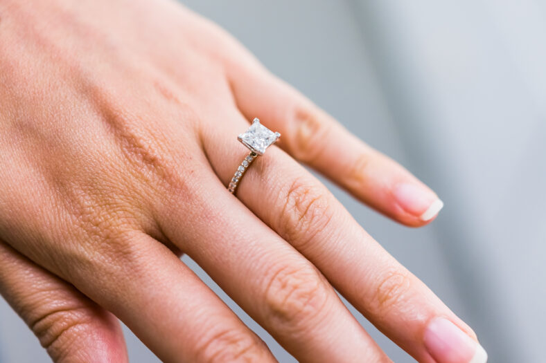 Macro closeup of princess cut diamond engagement ring on woman's female hand showing detail and texture