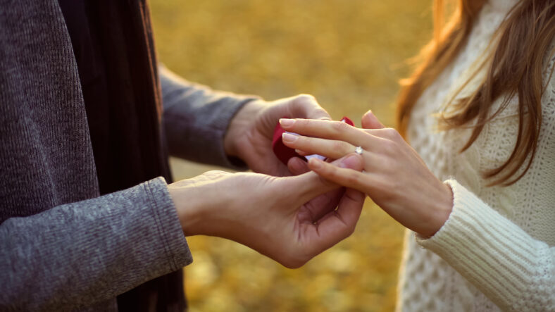 Guy putting beautiful diamond ring on finger of his bride, serious relationship