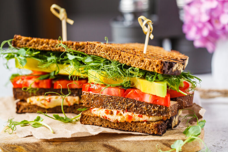 Vegan sandwich with tofu, hummus, avocado, tomato and sprouts on board.