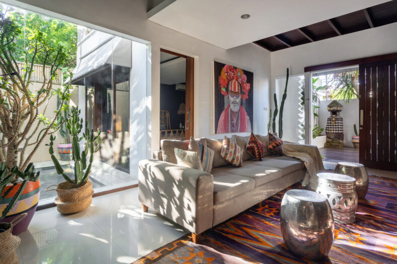 Living room in cozy house with stylish interior, ethnic decor, cushions on comfortable couch, woven ornamental carpet, cactus in wicker basket and artwork on wall