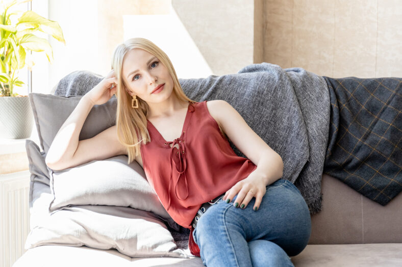 young blonde girl sitting on a sofa in a bright room and looking at the camera