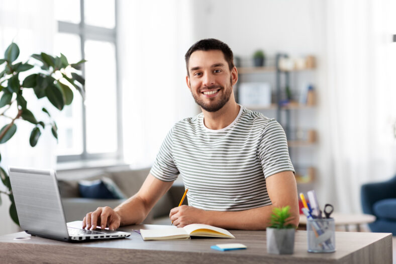 remote job, technology and people concept - young man with notebook and laptop computer working at home office