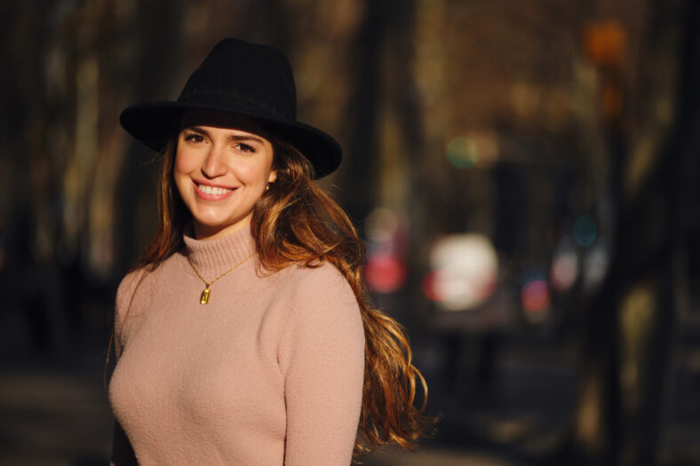 Portrait of a young woman looking at the camera and smiling while standing outdoors. Urban concept.