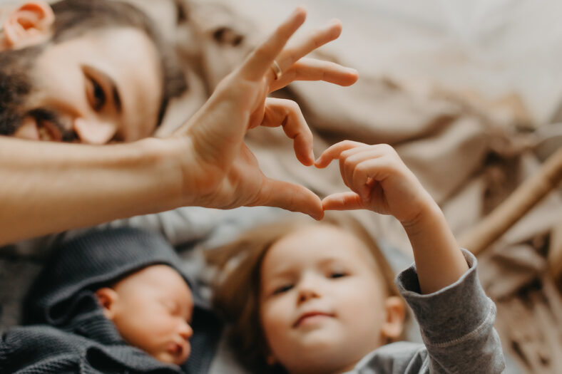 stylish bearded father kisses a sleeping newborn girl. Parent holding rocking child daughter son in hands. Authentic lifestyle parenting fatherhood moment. Dad family home life with 2 children