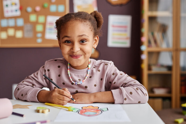 Cute successful learner of primary school looking at camera with smile