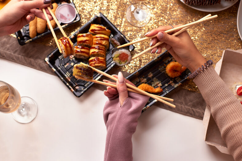 Portrait of three beautiful young women eating japanese food and drinking wine at home. Take away delivery