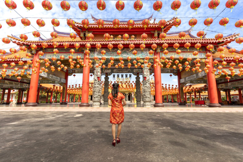 Asian woman in red cheongsam qipao dress is visiting the Chinese Buddhist temple during lunar new year for traditional culture concept