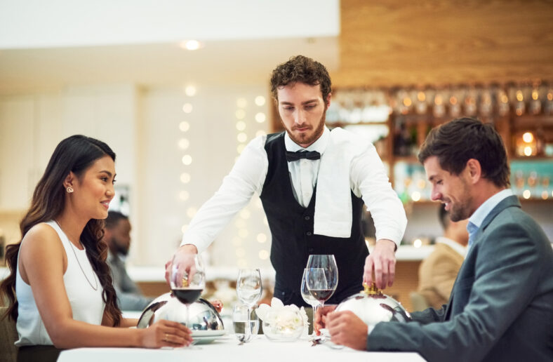 Couple, restaurant server and fine dining at table for valentines day date, bonding and romance in night. Man, woman and waiter with food, service and hospitality for dinner, love and celebration