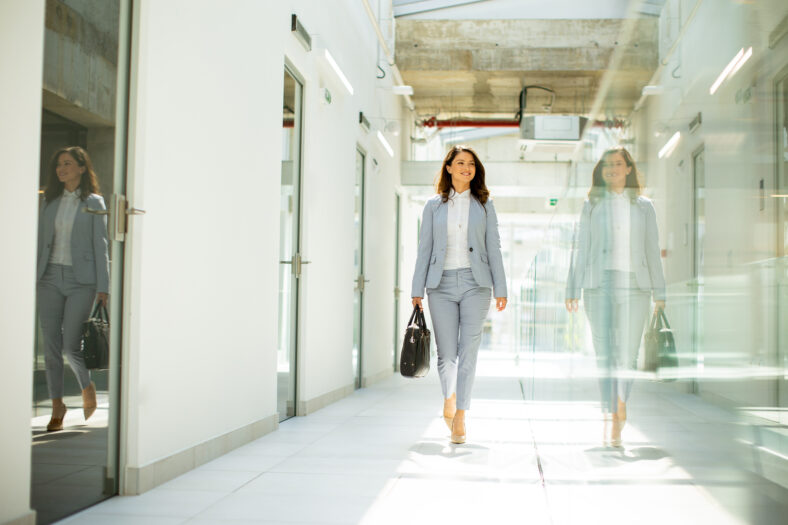 Pretty young business woman walking with briefcase in office hallway