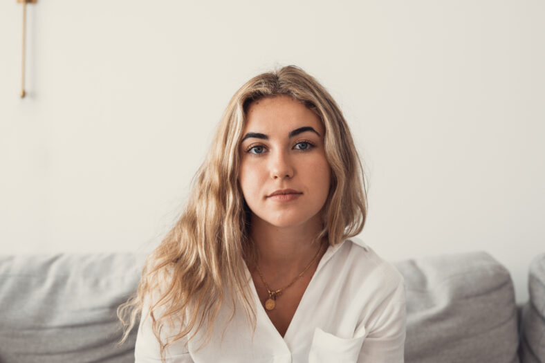 Positive serious millennial model girl home female head shot portrait. Beautiful young adult Caucasian woman looking at camera, posing in apartment. Front profile picture