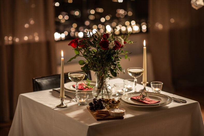 holidays, romantic date and celebration concept - close up of festive table serving for two with flowers in vase and candles burning at home on valentine's day