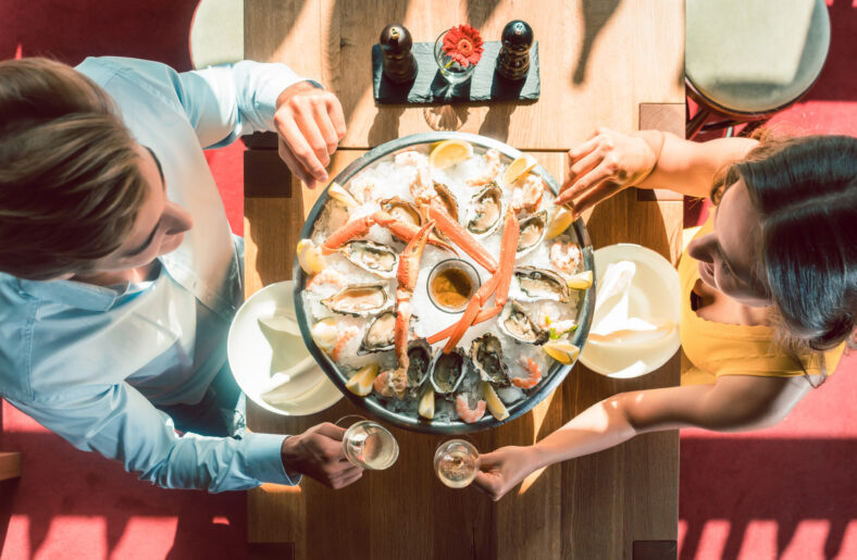 High-angle view of a happy young couple toasting with champagne during romantic dinner with fresh seafood at a trendy restaurant