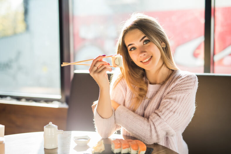 Woman eats traditional sushi rolls at the restaurant - close up photo.