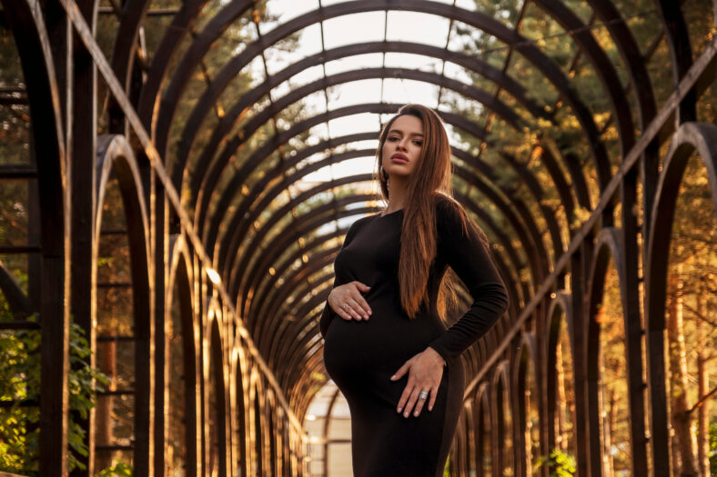 brunette pregnant woman in park. Summer day, sunset.