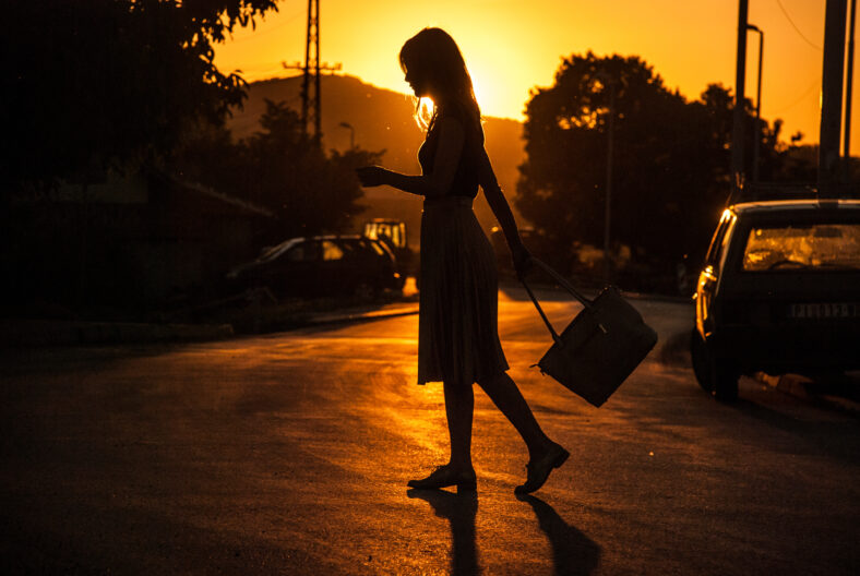 A silhouette of a woman walking on the street during a golden hour