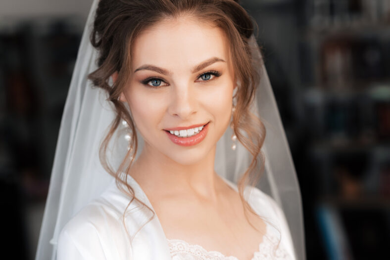 portrait of a beautiful bride with makeup and hair styling smiling during the morning preparation for the wedding