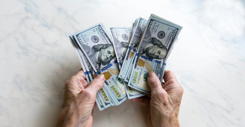 Close-up of an elderly woman's hands holding money in 100 dollar bills, compensation.