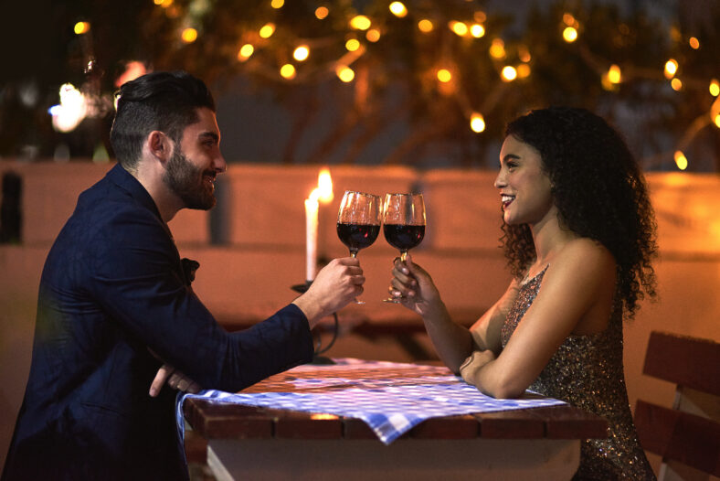 Love, wine and toast of couple on date for fine dining, restaurant or night valentine celebration together. Happy black woman with romance partner alcohol glass, celebrate and luxury in night bokeh.