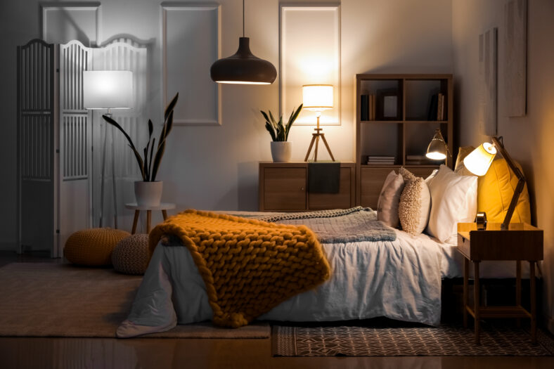 Interior of bedroom with knitted plaid on bed and glowing lamps at night